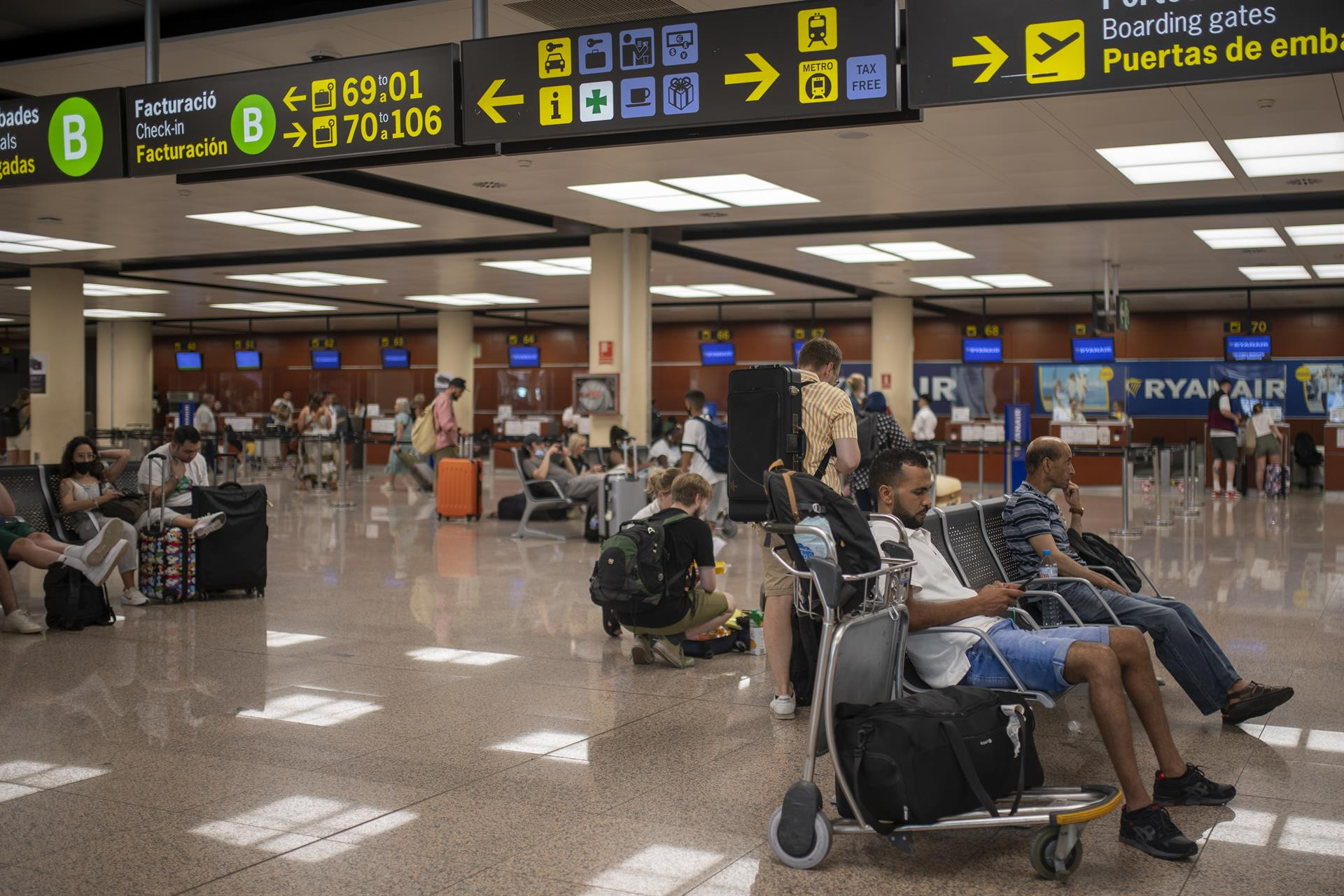 Varias personas esperan sentadas con sus maletas en el Aeropuerto Josep Tarradellas Barcelona-El Prat / EUROPA PRESS