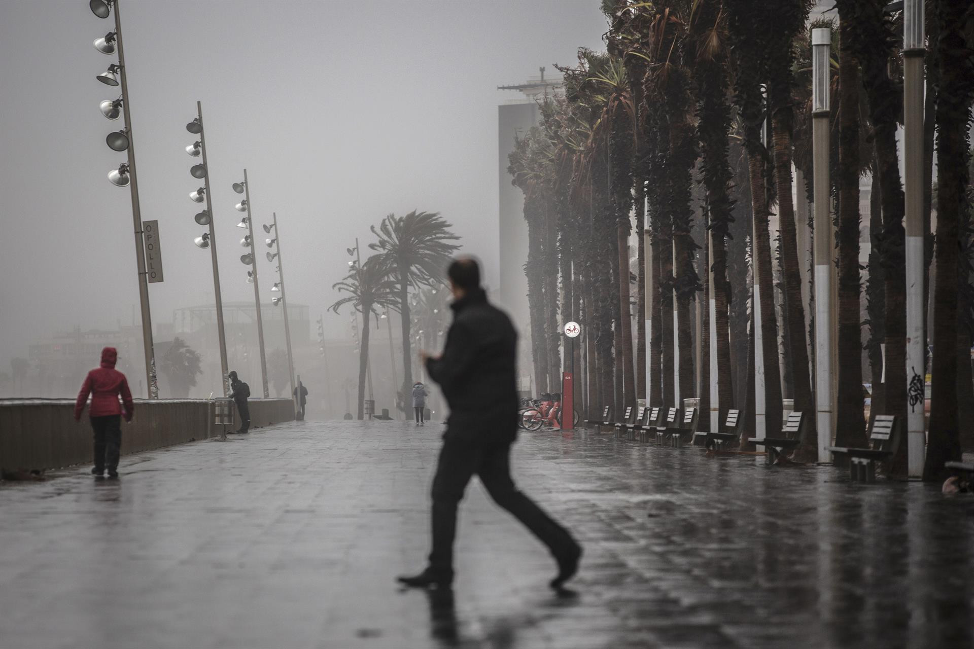 Un hombre camina por el paseo marítimo de Barcelona con lluvia / EUROPA PRESS - David Zorrakino