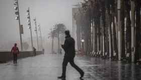 Un hombre camina por el paseo marítimo de Barcelona con lluvia / EUROPA PRESS - David Zorrakino