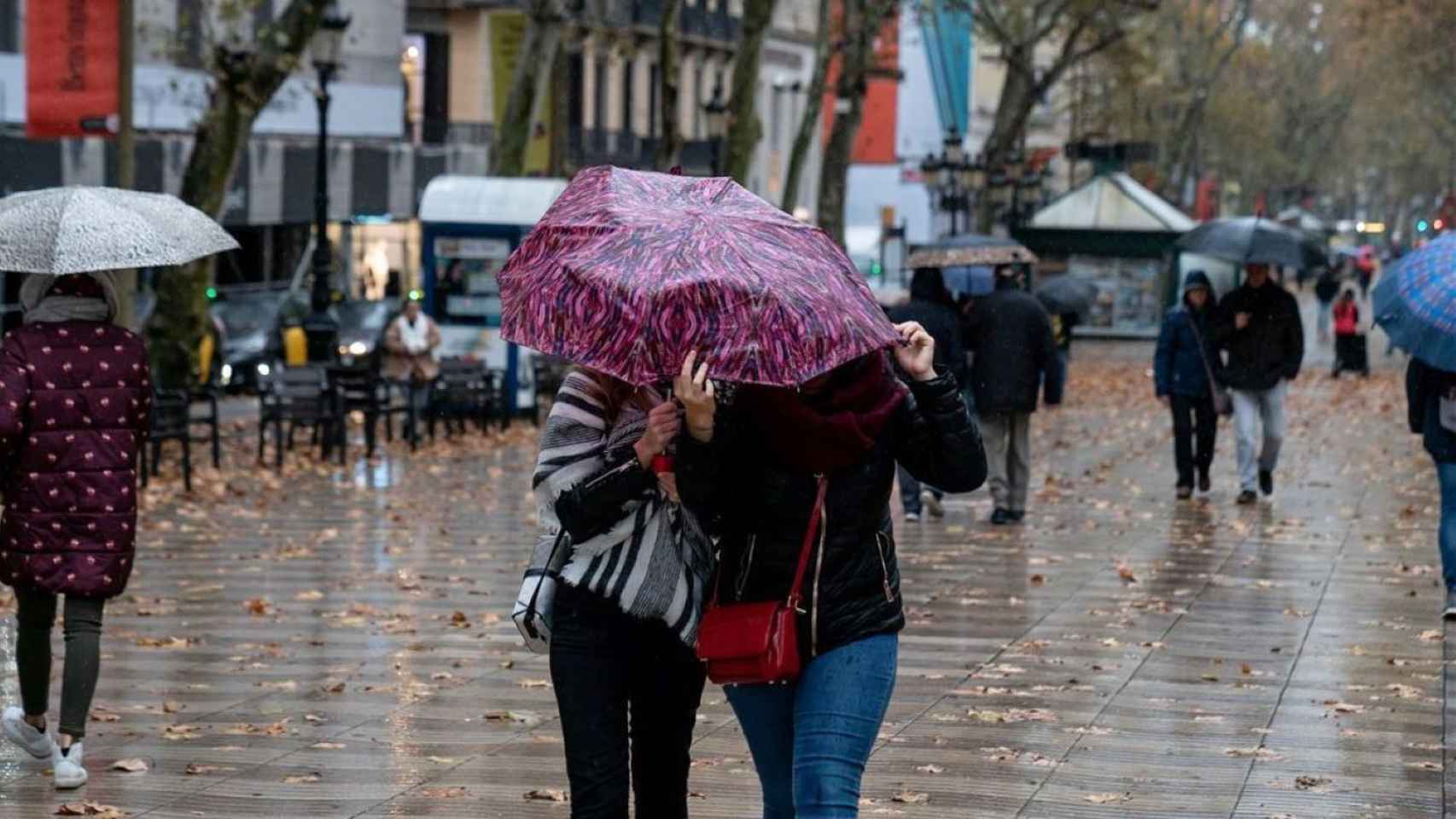 Dos ciudadanos se protegen de la lluvia en la Rambla de Barcelona / AJ BCN