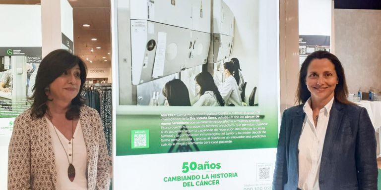 La doctora Cristina Iniesta y la investigadora Violeta Serra posan delante de la exposición / CG