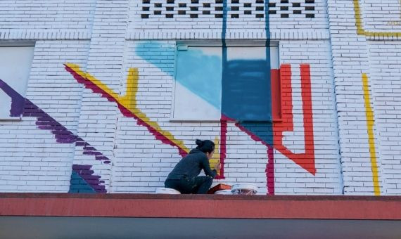 Una chica pintando el mural colectivo del barrio de la Cañada