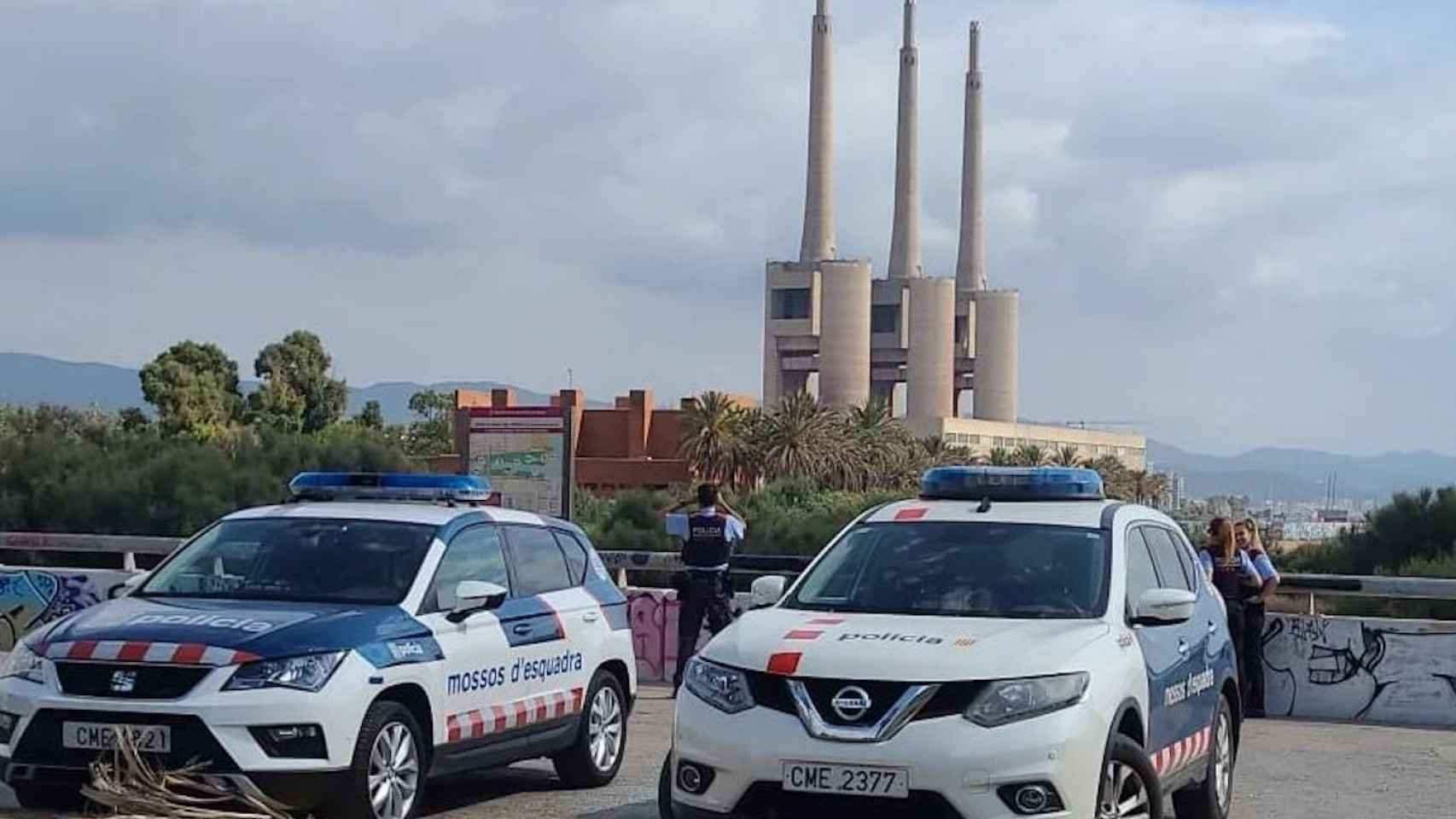 Dos coches de mossos con las chimeneas de Sant Adrià de fondo